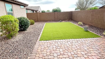 Un jardin avec une terrasse dallée, une pelouse et un mur en briques.