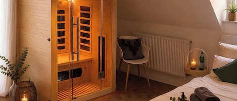 Un dormitorio con un armario de madera, una silla, una mesita de noche con una botella y una toalla enrollada.
