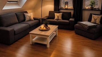 Una sala de estar moderna con piso de madera, dos sofás oscuros con almohadones decorativos, una mesa de centro y un tragaluz.