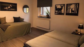 Un dormitorio con dos camas, ventana con vistas, radiador y decoración en la pared.