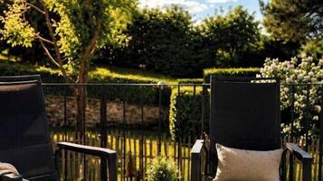 Un área de estar al aire libre con dos sillas y una mesa, rodeada por una cubierta de madera y una cerca de metal negro.