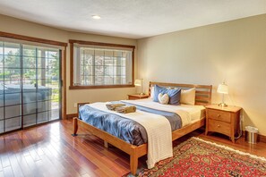 A bedroom with a large bed, wooden headboard, a nightstand, a lamp, a window with a view, and a patterned rug. - Dock + Hot Tub! Waterfront Lake Tahoe Getaway (South Lake Tahoe)