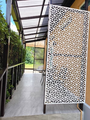 A corridor with a patterned screen, a tiled floor, and a view of greenery outside.