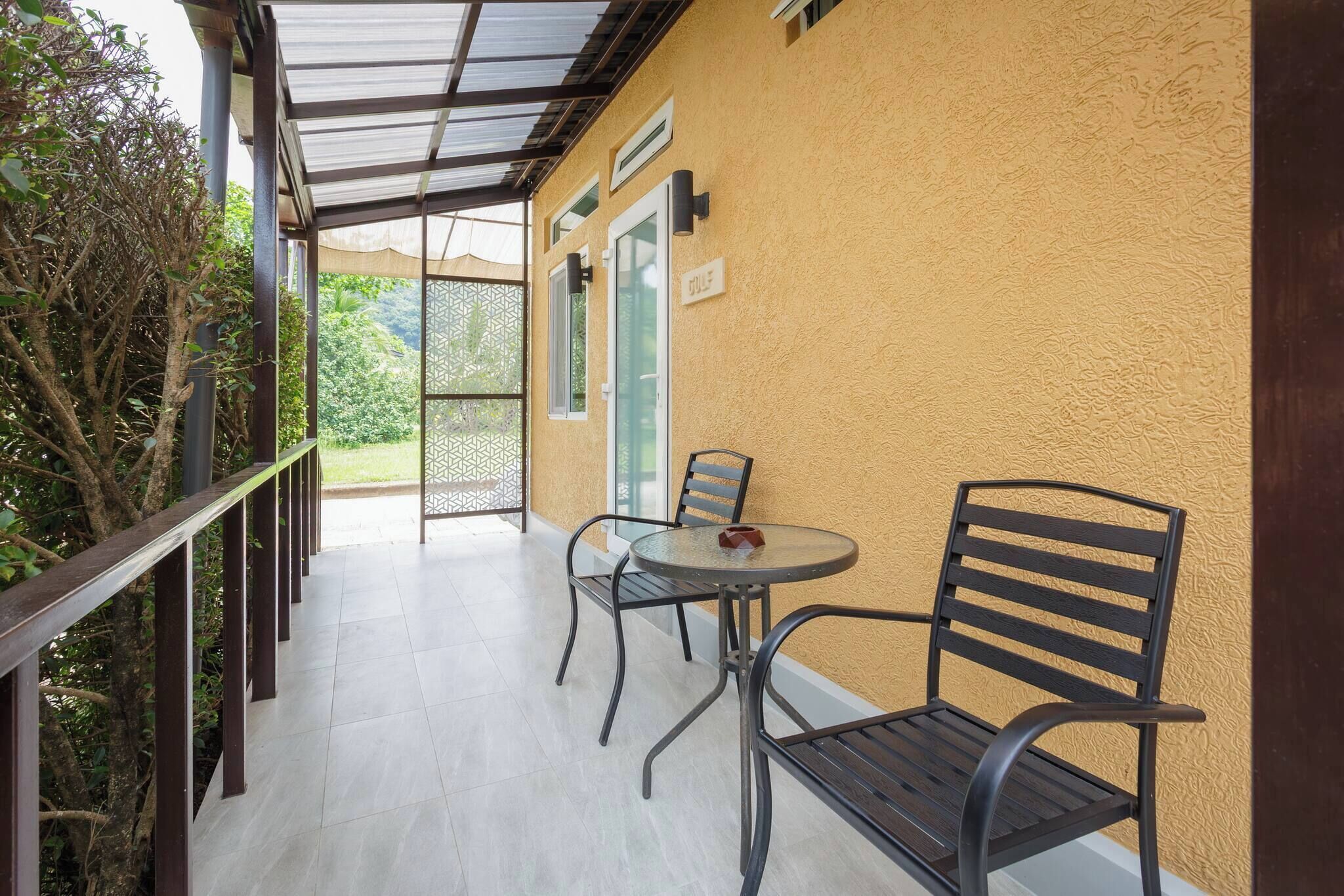 A covered outdoor area with a table and chairs, a wooden railing, and a yellow wall.