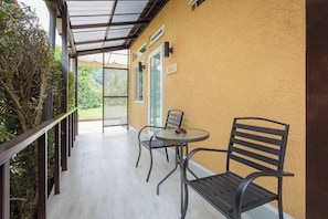 A covered outdoor area with a table and chairs, a wooden railing, and a yellow wall.