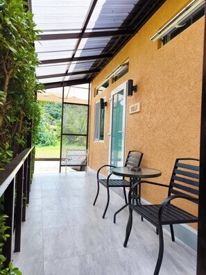 Eine überdachte Terrasse mit Tisch und Stühlen, eine Tür mit der Aufschrift 'GOLF' und Blick auf Grünflächen.