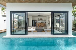 Una casa moderna con piscina, comedor y sala de estar con sofás y una mesa de centro.