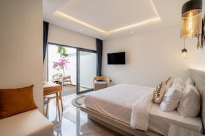 A modern hotel room with a bed, a seating area, a TV, and a balcony with a view. - Majys 1 Villa by Tasvan (Badung)