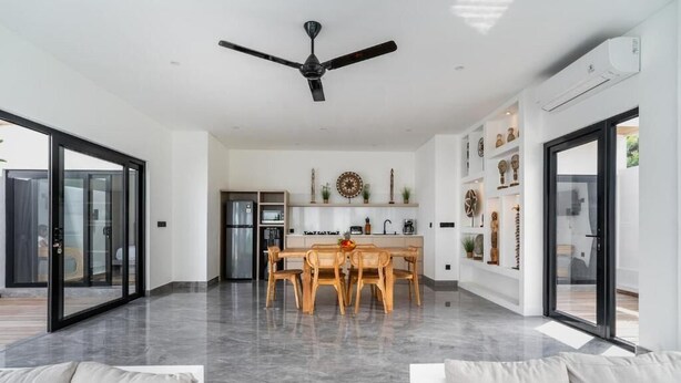 Een ruime woonkamer met een eettafel, een plafondventilator en een keuken op de achtergrond.