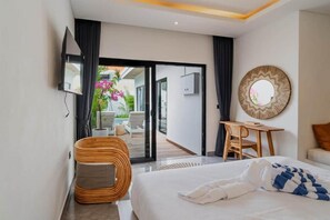 Habitación de hotel con cama, escritorio, silla, televisión y vista a un área exterior con mesa y sillas.