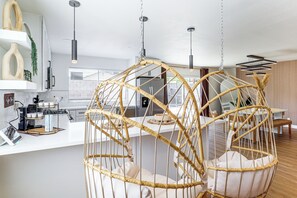 A modern kitchen with a coffee station, hanging light fixtures, and a dining area with a rattan chair. - Grand Prix Calm at the Vegas Zen Den (Las Vegas)