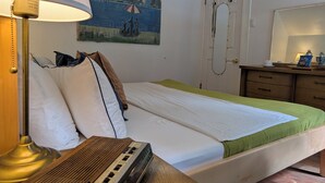 A hotel room with a bed, a lamp, a painting, a mirror, and a wooden dresser. - Vrbo Property (Staten Island)