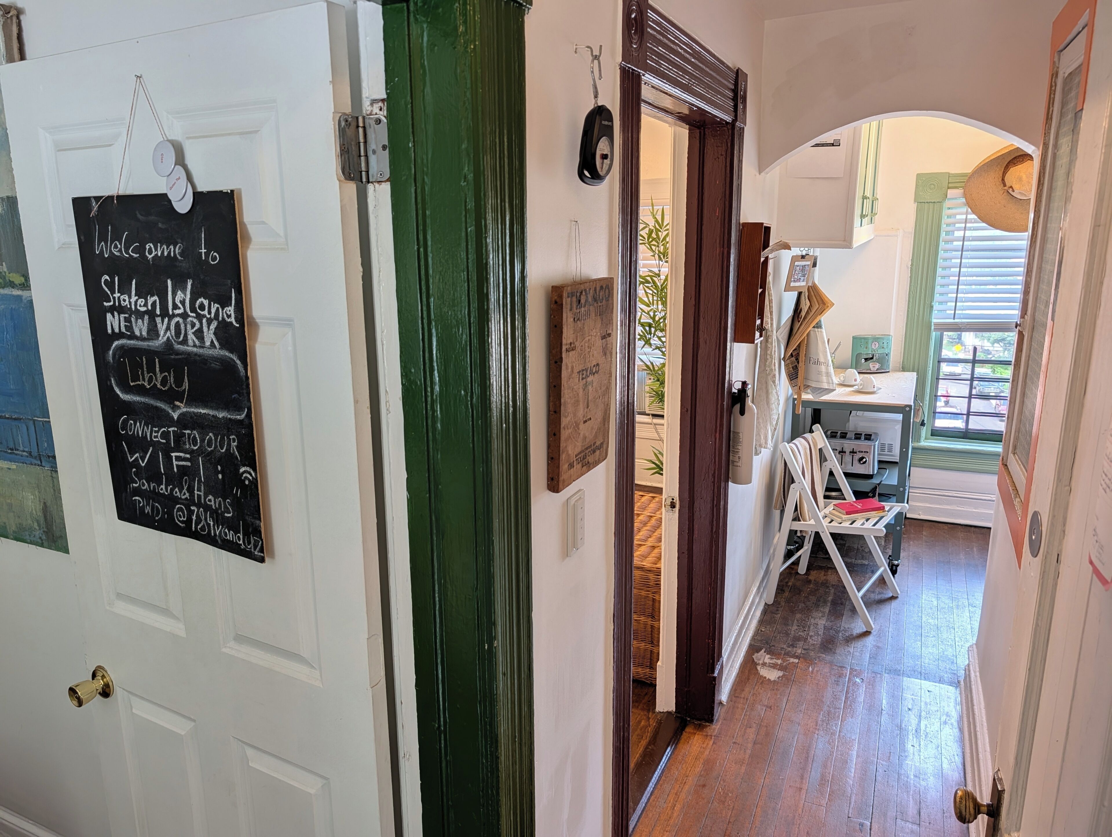 A hallway with a chalkboard sign, a door, and a glimpse of a room with a window and a table.
