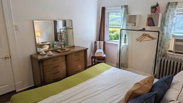 A bedroom with a bed, a dresser, a mirror, a window with curtains, and a radiator.