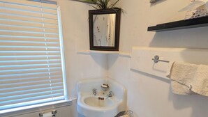 A bathroom with a toilet, sink, mirror, and a window with blinds. - Vrbo Property (Staten Island)