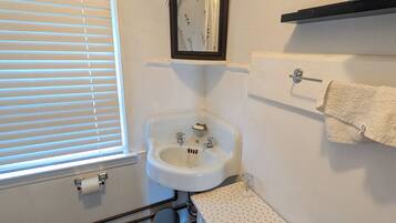 A bathroom with a toilet, sink, mirror, and a window with blinds.