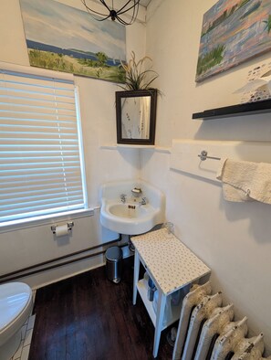 Un baño con inodoro, lavamanos, espejo y ventana con persianas.