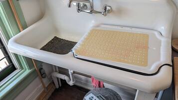 A white bathroom sink with a soap dish, a sponge, and a trash bin with a label.