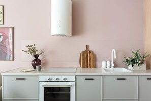 A kitchen with a white stove, oven, and sink, a wooden cutting board, a vase with flowers, and a potted plant.