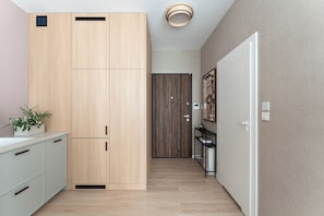 A hallway with a wooden wardrobe, a small plant, a door with a picture, and a shelf with items.