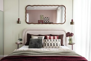 Ein Schlafzimmer mit einem Bett, Kissen, einem Spiegel und Nachttischen.