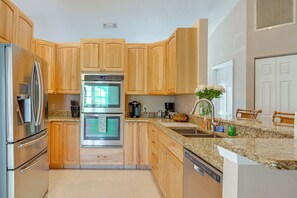 A modern kitchen with wooden cabinets, stainless steel appliances, a granite countertop, and a built-in dishwasher. - Private Hot Tub & Dock! Hutchinson Island Retreat (Fort Pierce)