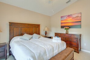 Ein Schlafzimmer mit einem großen Bett, einem Holzschrank, einem Nachttisch, einer Lampe und einem Gemälde, das einen Sonnenuntergang zeigt.