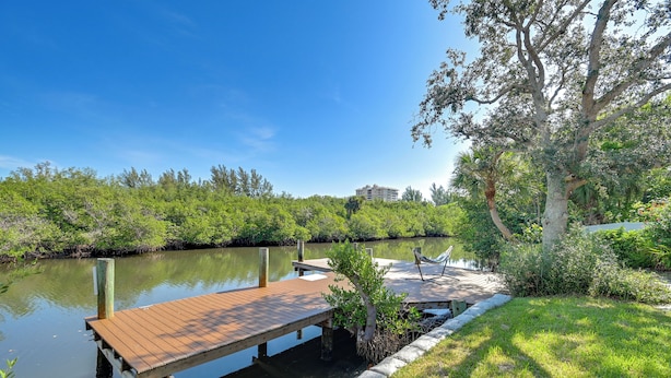 Une jetée en bois s’étendant sur une étendue d’eau calme, entourée d’une végétation luxuriante et sous un ciel bleu clair.