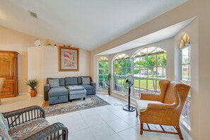 Ein geräumiges Wohnzimmer mit einer Couch, Sesseln, einem Ventilator und großen Fenstern mit Blick ins Freie.