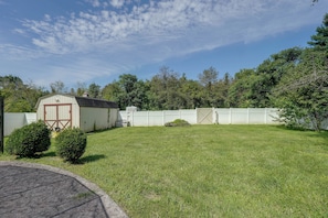 A fenced backyard with a shed, a well-maintained lawn, and dense trees in the background.