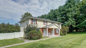 A two-story house with a front porch, a small garden, and a white fence. - Patio + Yard: Extended Escape in Hudson Valley! (Highland)