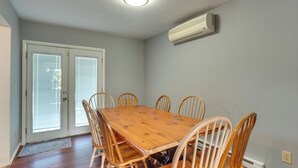 A dining room with a wooden table and six chairs, a sliding glass door, and a wall-mounted air conditioner. - Patio + Yard: Extended Escape in Hudson Valley! (Highland)