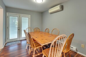 Een eetruimte met een houten tafel en zes stoelen, een schuifpui en een wandgemonteerde airconditioner.