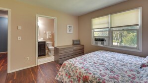 A bedroom with a wooden dresser, a bed with floral bedding, a window with blinds, and a view of trees outside. - Patio + Yard: Extended Escape in Hudson Valley! (Highland)