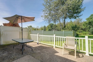 A patio with a table and an umbrella, a white fence, and a tree in the background.