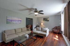 A living room with a ceiling fan, two sofas, a glass coffee table, and a dining area with chairs.