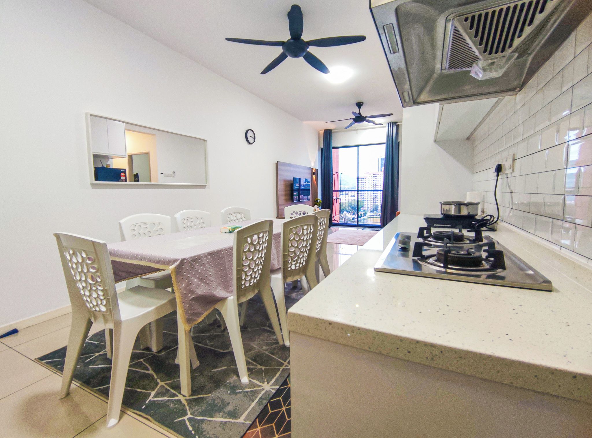 Une cuisine compacte équipée d’une cuisinière à gaz, d’un ventilateur de plafond et d’un coin repas avec une table et des chaises.