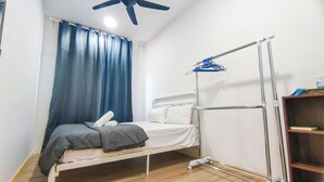 Una cama individual con estructura metálica, un ventilador de techo, una cortina azul y un estante metálico con escalera.