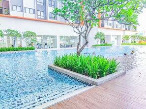 A swimming pool with a tiled edge, surrounded by greenery and a wooden deck. - Modern Loft at Residensi Rampai 2 by HCK (Kuala Lumpur)