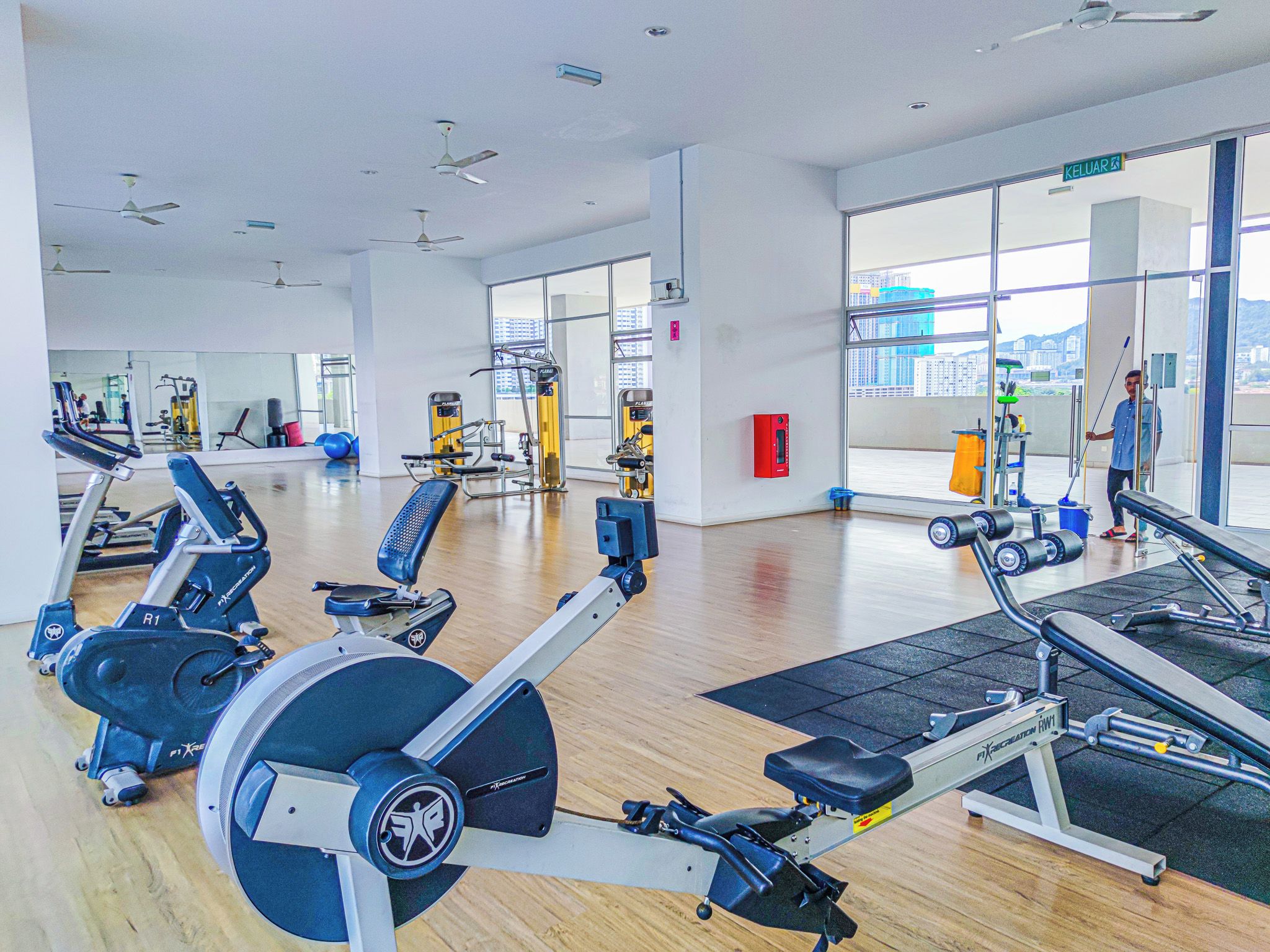 A modern gym with various exercise equipment, large windows, and a city view.