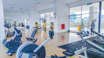 A modern gym with various exercise equipment, large windows, and a city view.