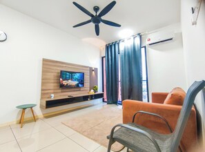 A modern living room with a flat-screen TV mounted on a wooden panel, a ceiling fan, a sofa, a chair, and a small table. - Modern Loft at Residensi Rampai 2 by HCK (Kuala Lumpur)