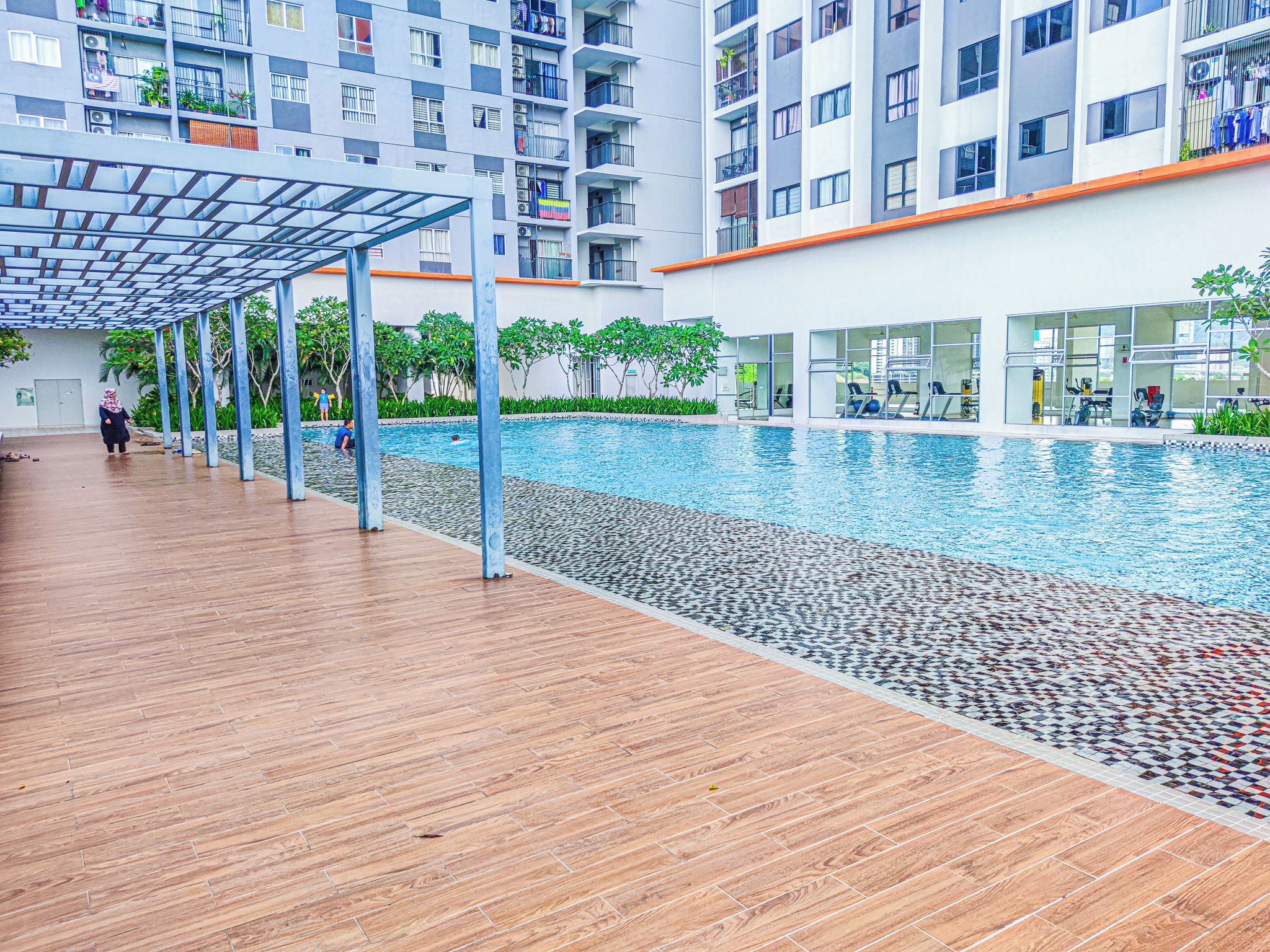 A modern indoor swimming pool with a wooden deck, surrounded by residential buildings.