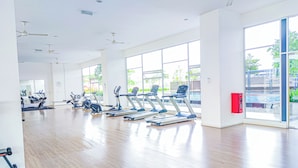 Un gimnasio amplio con cintas de correr y equipo de ejercicio, ventanas grandes y ventiladores de techo.