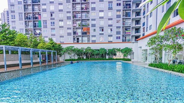 Una piscina con agua cristalina azul, rodeada por un edificio moderno con balcones y una zona de estar cubierta.