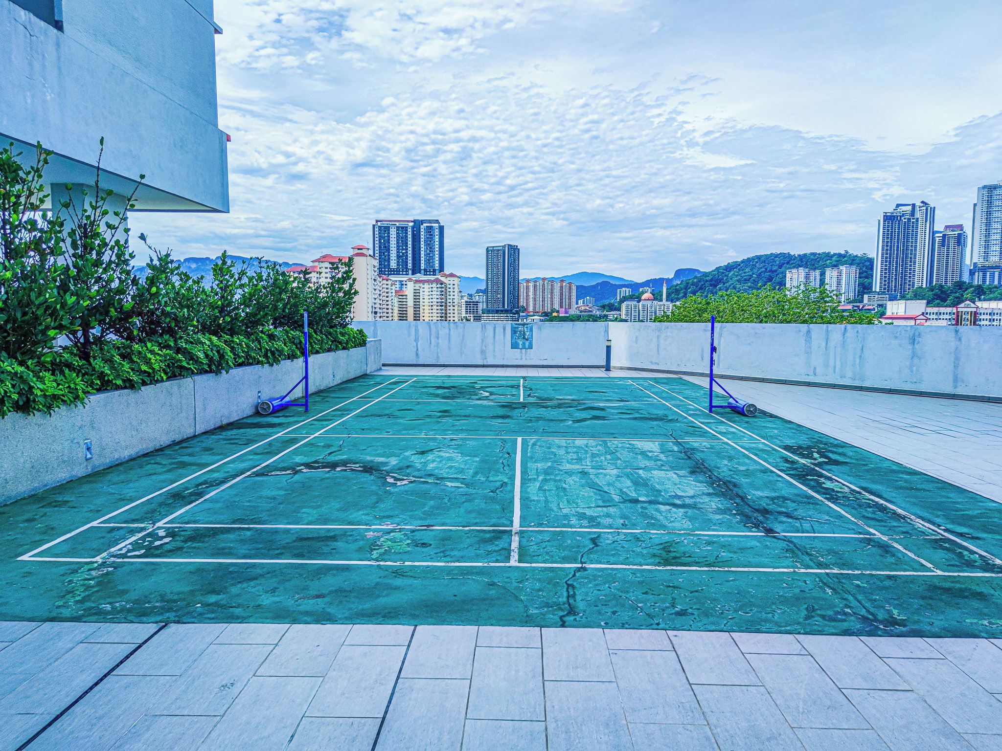 Ein Tennisplatz auf dem Dach mit Blick auf die Stadtlandschaft, umgeben von Grünflächen und modernen Gebäuden.