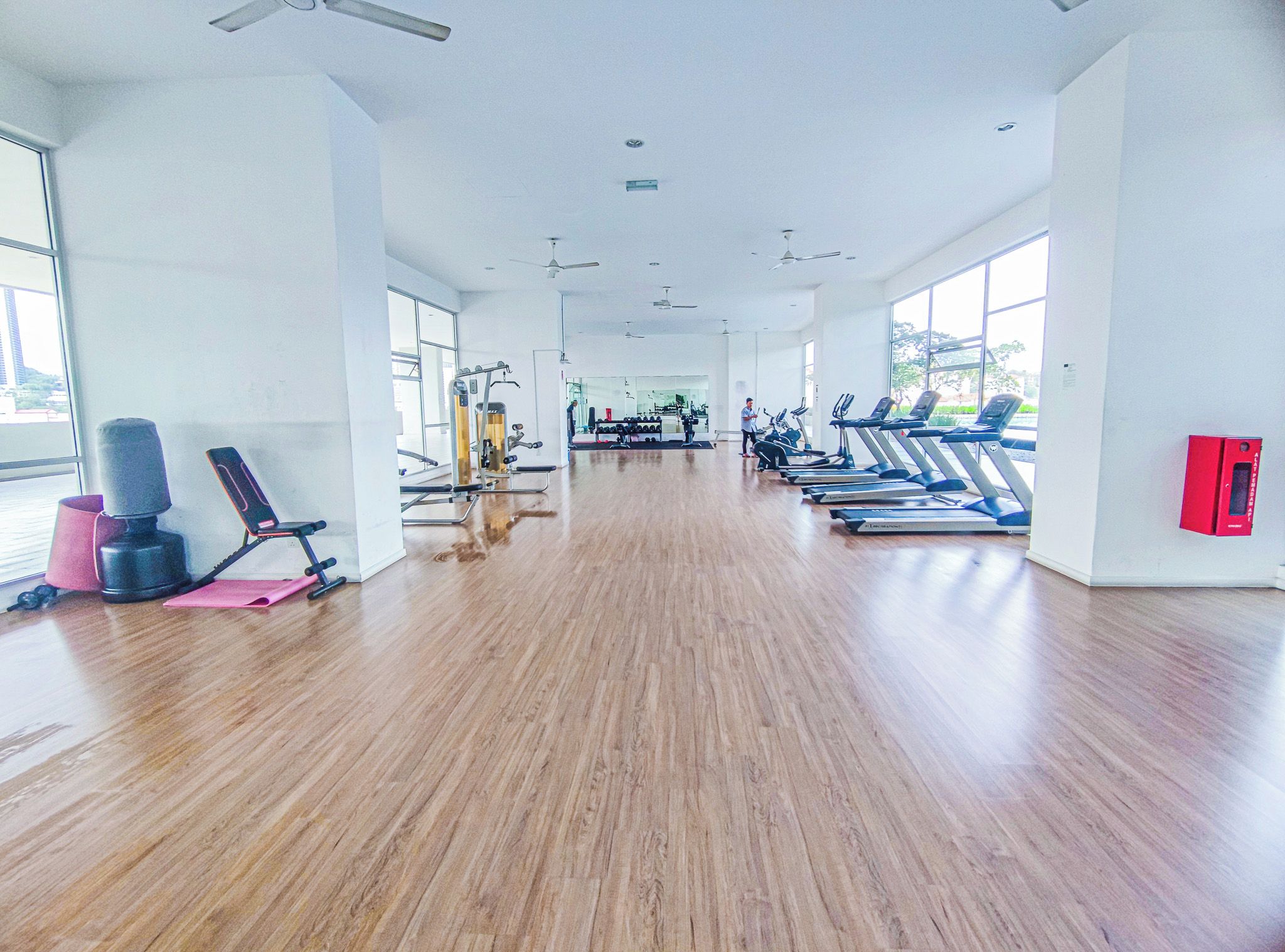 A spacious gym with exercise equipment, large windows, and a wooden floor.