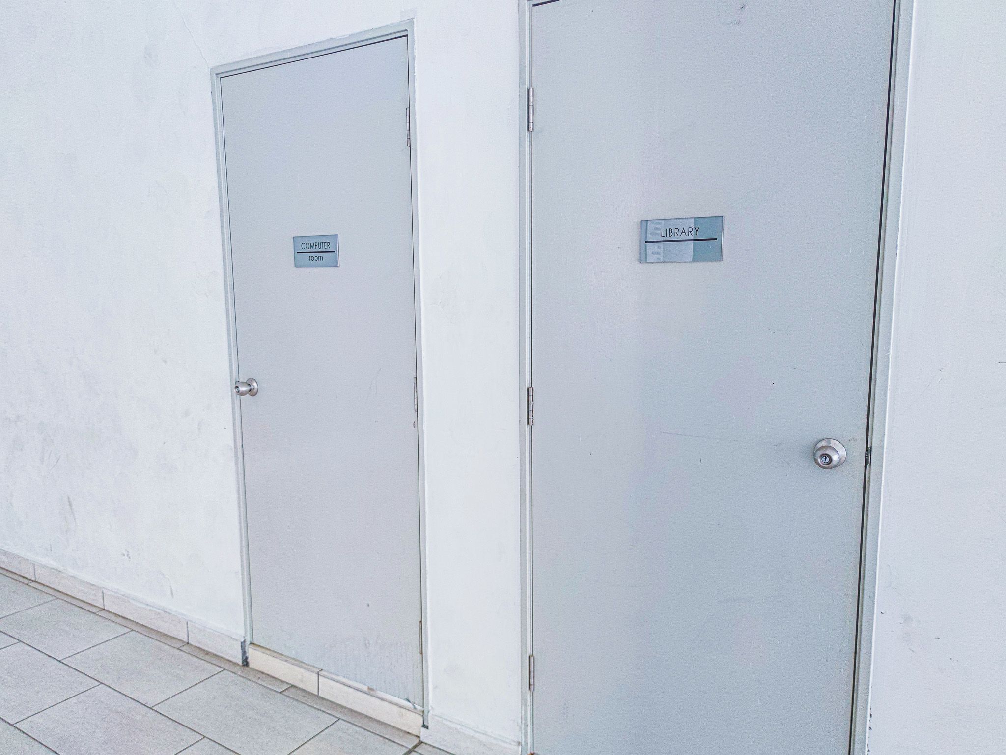 Deux portes métalliques, chacune portant une étiquette indiquant qu’il s’agit d’une salle informatique et d’une bibliothèque.
