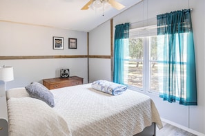 A bedroom with a bed, a nightstand, a fan, and a window with curtains. - Fishing Pond & Patio Near Lake Texoma! (Kingston)