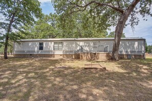 A single-story mobile home with a brick foundation, a front porch, and a large tree to the right. - Fishing Pond & Patio Near Lake Texoma! (Kingston)